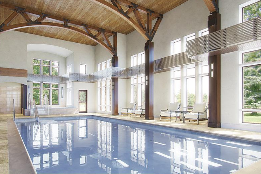An indoor swimming pool in a large, elegant building with high wooden ceiling beams, tall windows, and lounge chairs along the poolside.